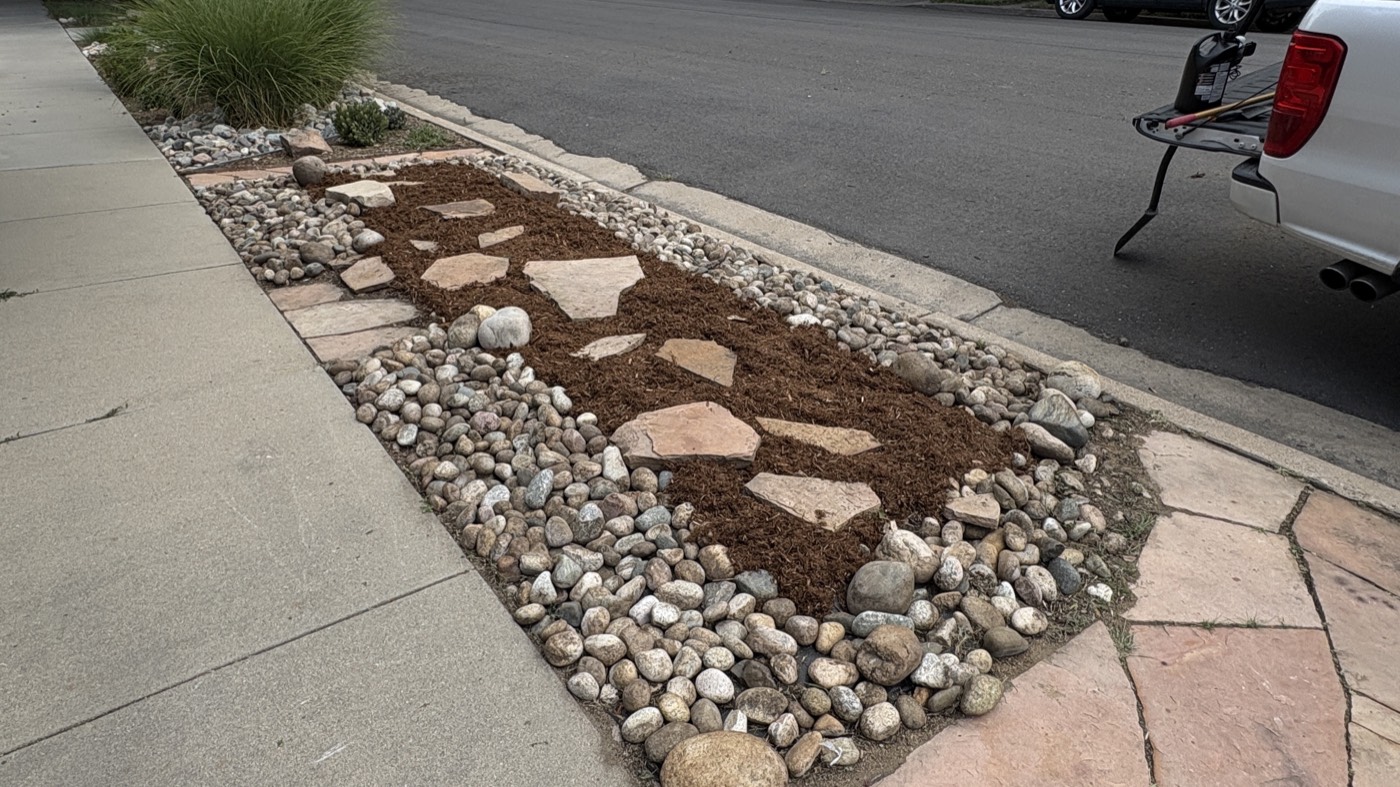 Flagstone and mulch bed with a river-rock border along a parking strip