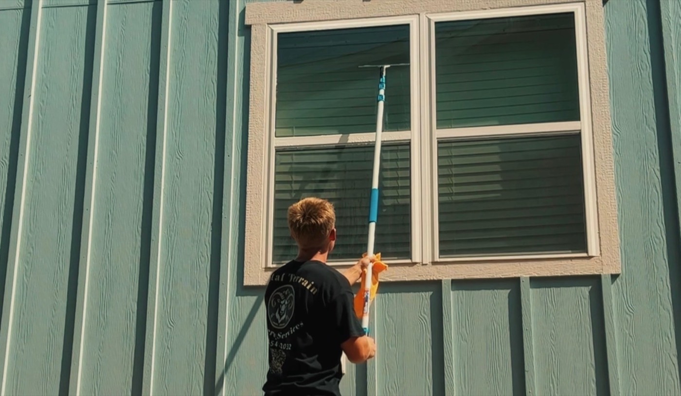 Total Terrain crew member cleaning an exterior window with an extension pole